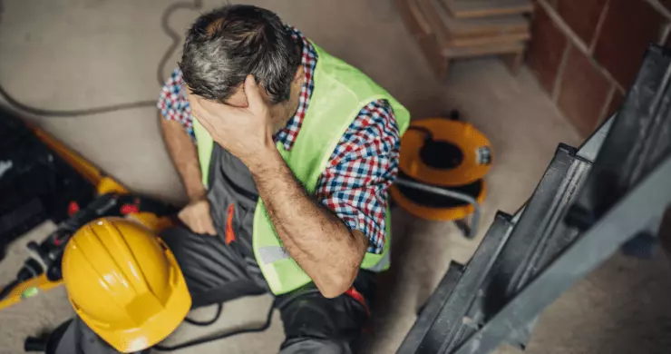 Elagueur professionnel avec son gilet et son casque posé, blessé et assis à coté de son échelle de travail